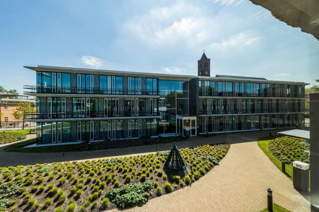 Modern kantoorgebouw aan de De Cuserstraat 85 met glazen gevel en aangelegde voortuin.